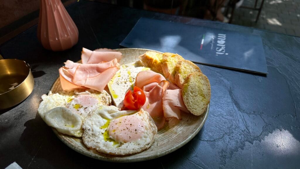 Photo of plate of various foods, turkey ham, eggs, feta cheese, a small tomato, and bread.