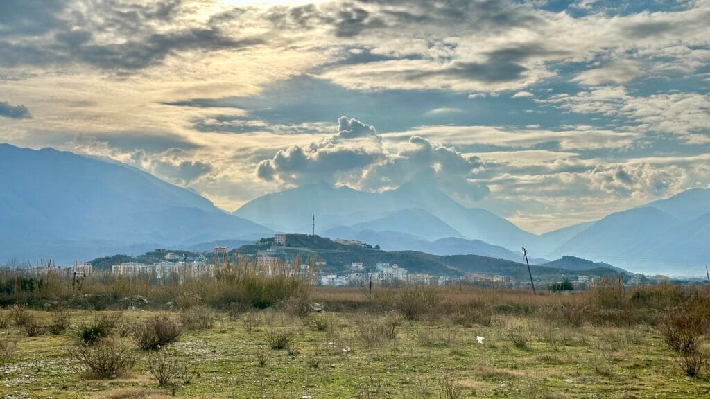 photo from the roadside in southern Albania. Showing clouds over a mountain range, with sunshine coming down from above.